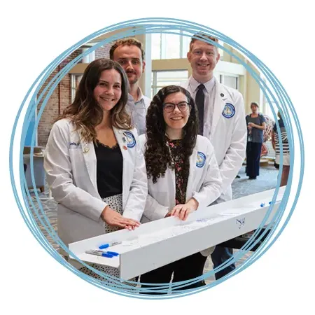 Four C O M students stand in front of a ceremonial beam they signed to celebrate the upcoming Harold and Bibby Alfond Center for Health Sciences on the Portland Campus